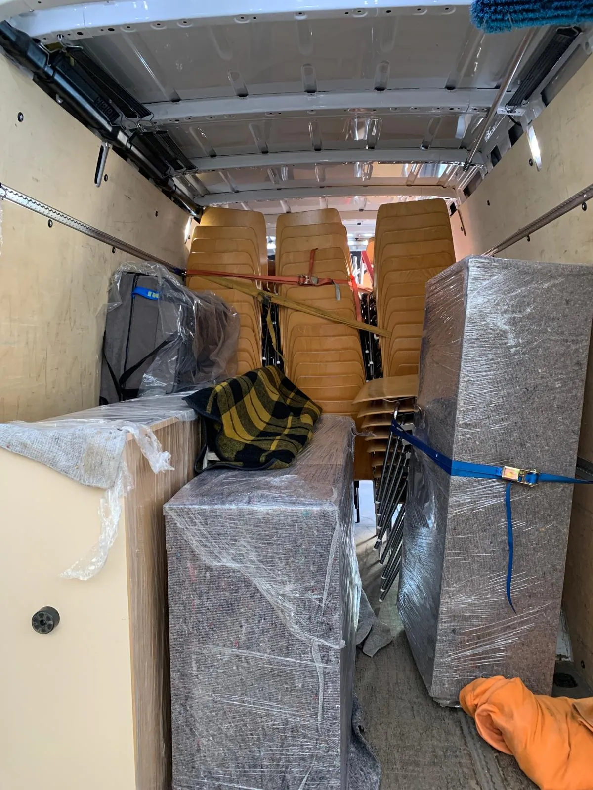 Sicht in den Innenraum eines Transporters mit gestapelten, gepolsterten Stühlen, mehreren verpackten Möbelstücken und umzugsdecken.