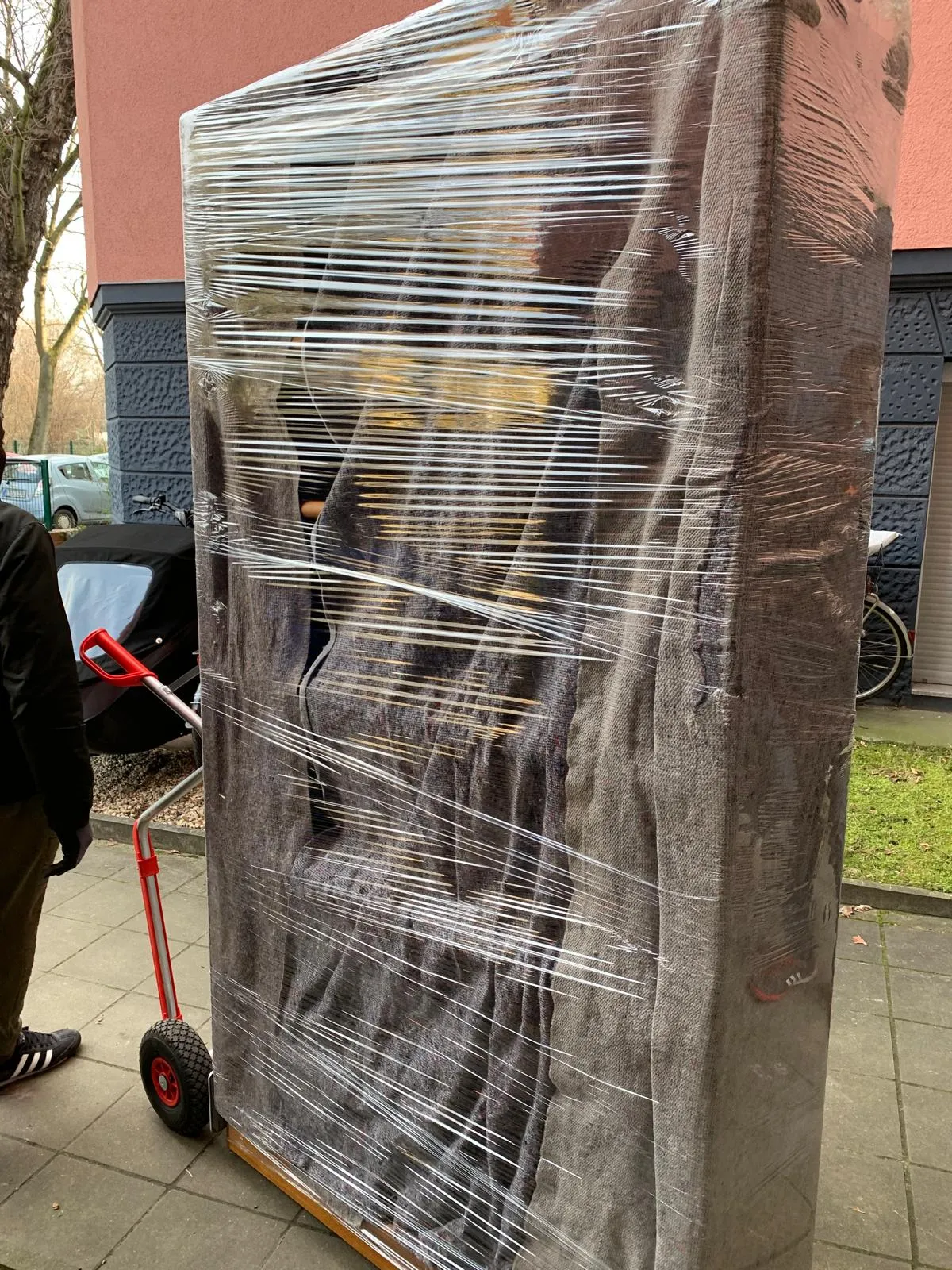 Mit Schutzfolie umwickelte, gepolsterte Möbel auf einem Sackkarre vor einem Wohnhaus.
